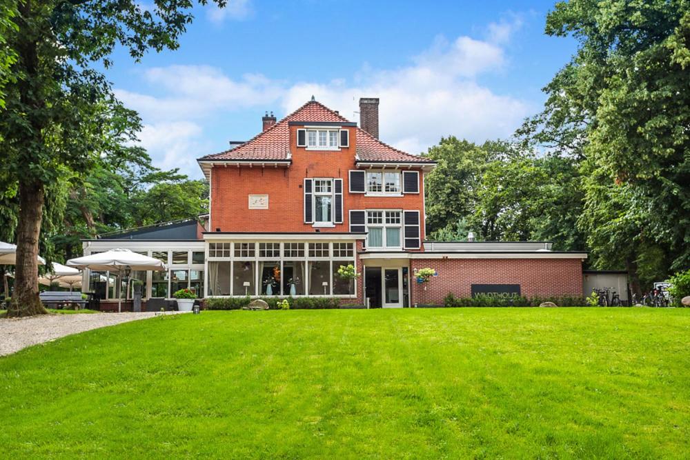 een groot rood bakstenen huis met een groen gazon bij Hotel & Restaurant Wildthout in Ommen