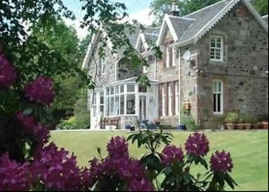 a large stone house with purple flowers in front of it at Glebe Country House Tarbet in Arrochar