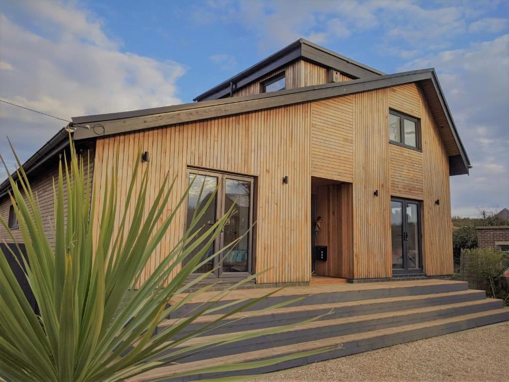 a wooden house with a palm tree in front of it at Cranmer - New Eco Beach House 4 Bed HOT TUB & Bikes in Camber