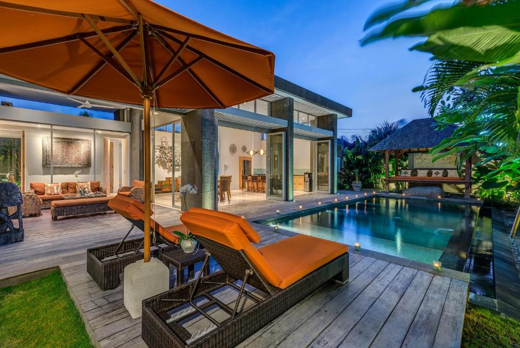 a home with a pool and a patio with orange chairs and an umbrella at Aramanis Villas in Seminyak