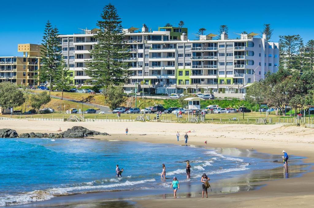 un grupo de personas en una playa con edificios en el fondo en Sandcastle Apartments, en Port Macquarie