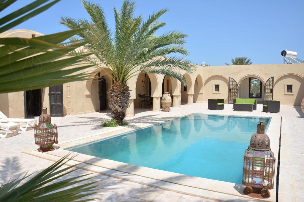 a swimming pool with a palm tree next to a building at Dar Almassa in Mellita