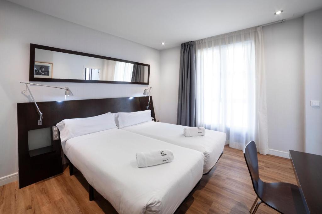 Habitación de hotel con 2 camas blancas y escritorio. en Petit Palace Arana Bilbao en Bilbao