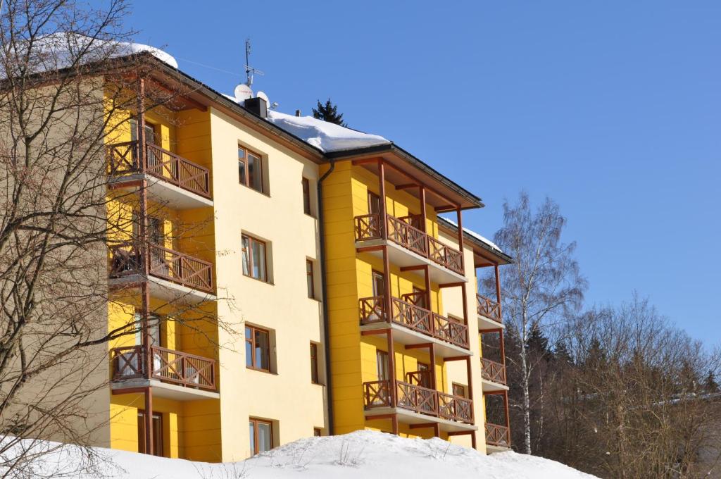 a yellow apartment building with snow on the ground at Apartman Kamila in Janske Lazne