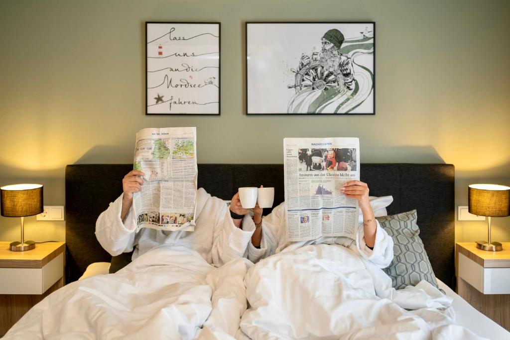 uma pessoa deitada na cama a ler jornais em Stadthotel Jever em Jever