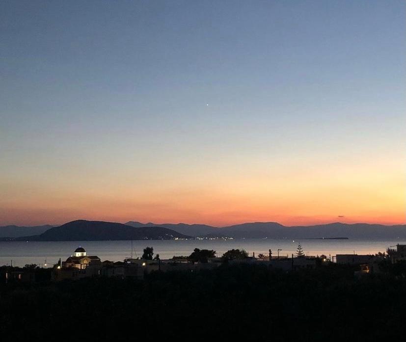 una puesta de sol sobre un cuerpo de agua con montañas en el fondo en Pepper Tree, en Aegina Town