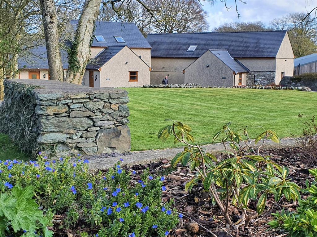 a house with a stone wall and flowers in a yard at Fodol Cottages in Menai Bridge