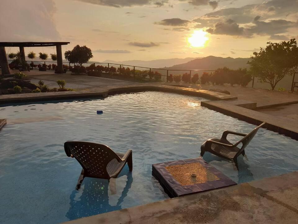 a pool with two chairs in the water with the sunset at Casa campestre Finca la Roca in La Mesa