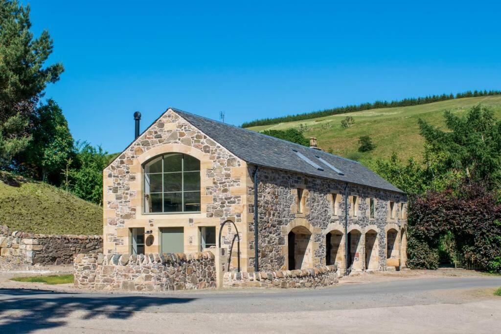 a stone building with a large window on a hill at Woodmill Arches - Designer Barn Conversion for Two in Lindores