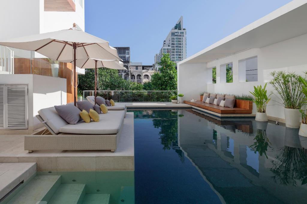 a pool with a couch and an umbrella next to a house at twothree a homely hotel - SHA Extra Plus in Bangkok