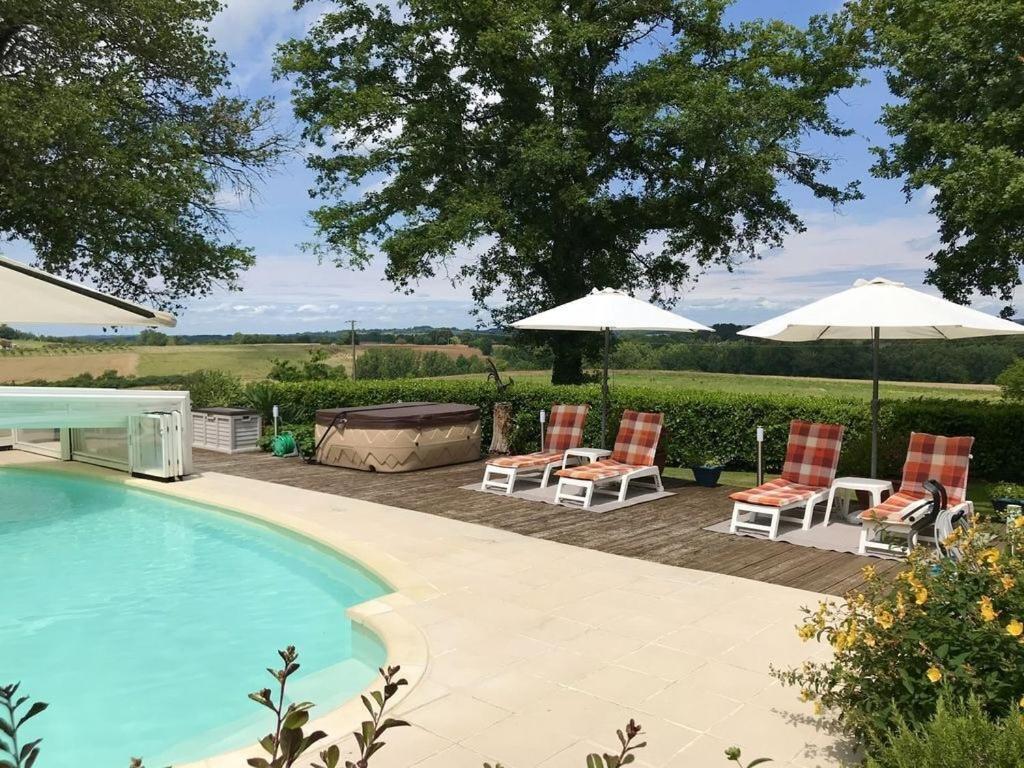 a swimming pool with two chairs and umbrellas next to at Private Gite with heated pool with retractable cover and hot tub in Cendrieux
