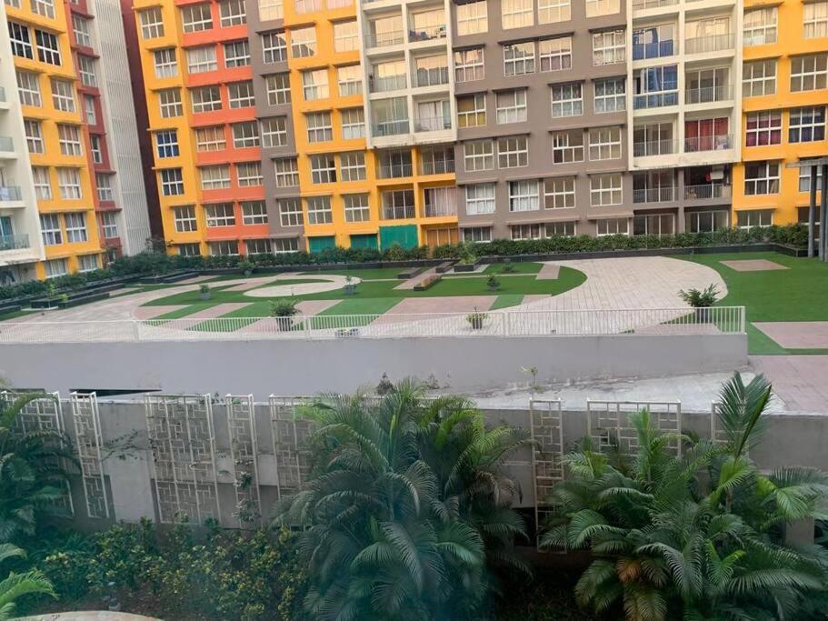 dos fotos de un edificio con palmeras y edificios en Garden View 1 BHK2BR Appt., Rio De Goa TATA Housing, en Sancoale