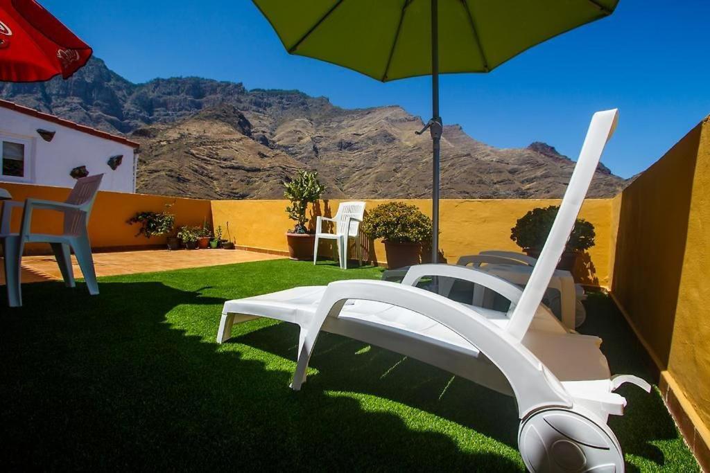 Solarium Agaete Valley Retreat 3-BR في أَغايتي: كرسي أبيض ومظلة على عشب