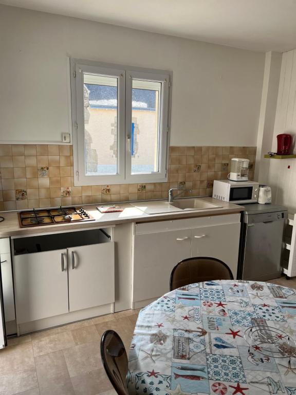 a kitchen with white cabinets and a table and a sink at Petite maison au coeur du village in Mesquer