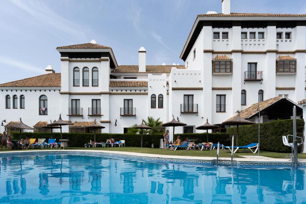 une piscine en face d'un grand bâtiment blanc dans l'établissement Moon Dreams El Cortijo, à Matalascañas