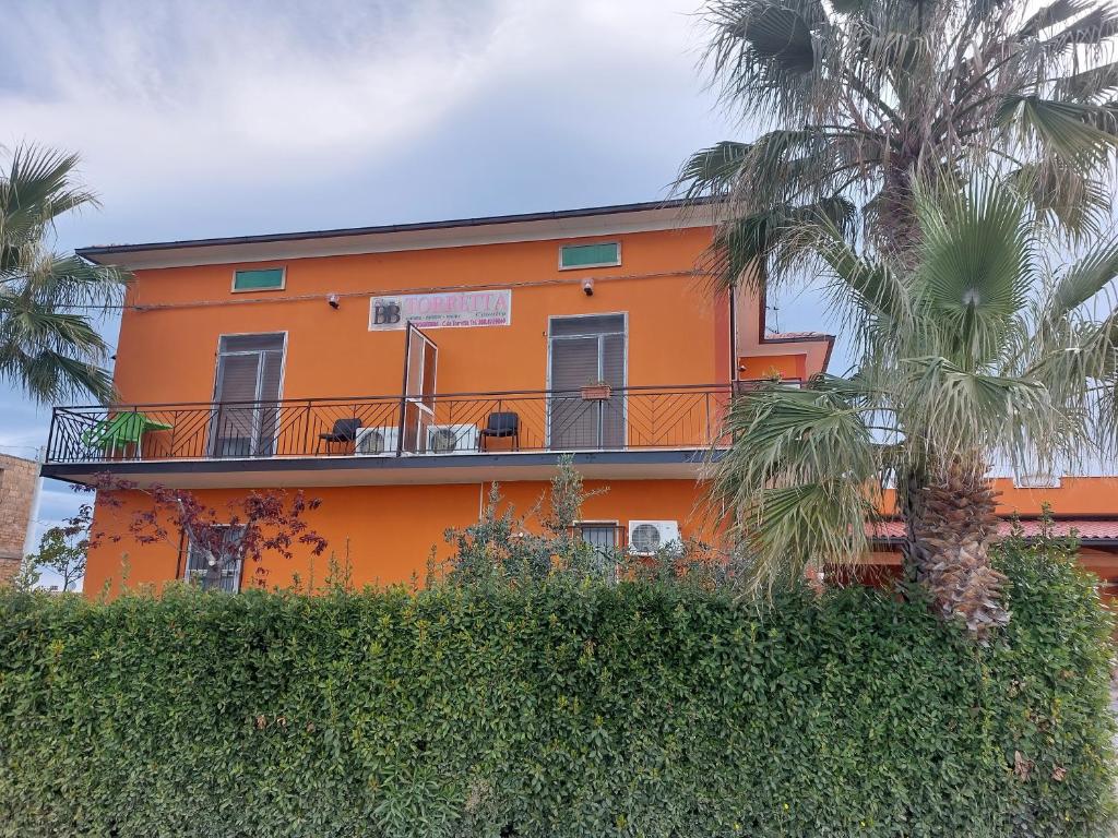 an orange house with a balcony and palm trees at Bed And Breakfast Torretta in Controguerra