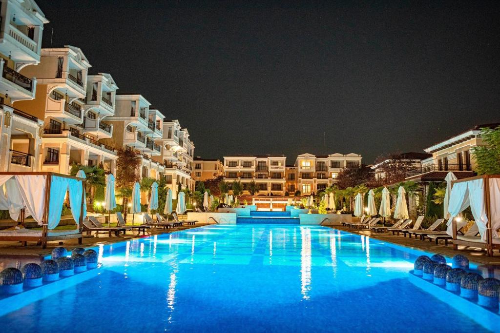 a large swimming pool with chairs and buildings at night at Niya Apartments Kavaci Sozopol GREEN LIFE in Sozopol