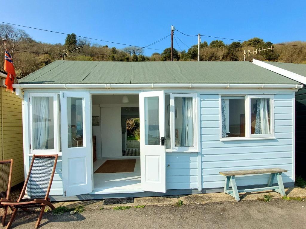 a blue tiny house with a porch and a bench at Sea Forever - Beautiful Chalet which Overlooks the Sea! Amazing Views,Lovely Interior and Set Within the Best Part of Lyme with Beaches, Restaurants and Harbour all on your Doorstep! Rated Highly in Lyme Regis
