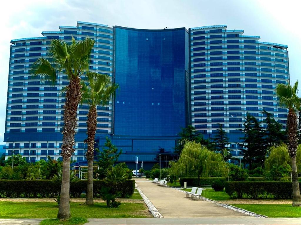 a tall blue building with palm trees in front of it at Grand Bellagio Batumi Convention & Casino Hotel in Batumi