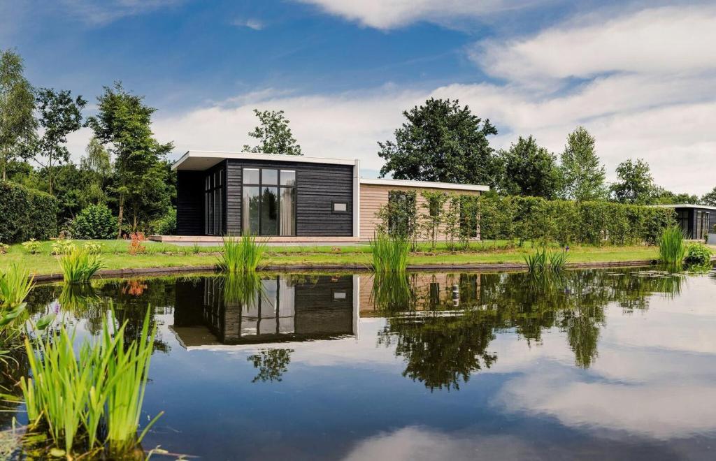 uma casa modular preta ao lado de um lago em Forest lodge with hot tub - 4 people em Rijssen