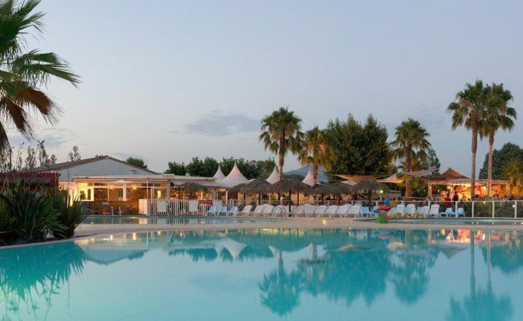 a large swimming pool with white chairs and palm trees at Mobil-Home 2 chambres camping 4 étoiles in Fréjus