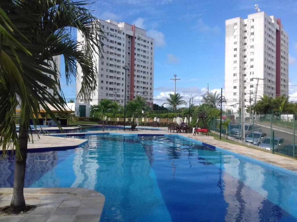 a large swimming pool with a palm tree and buildings at Piatã apartamento com Clube in Salvador