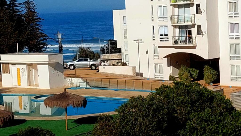 a building with a swimming pool next to the ocean at Acogedor Departamento en El Tabo in El Tabo