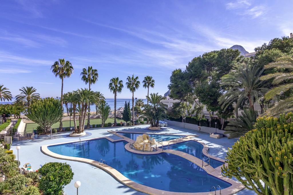 a large swimming pool with palm trees and the ocean at Villas Guzman - Apartamento Trond Paraiso Mar in Calpe