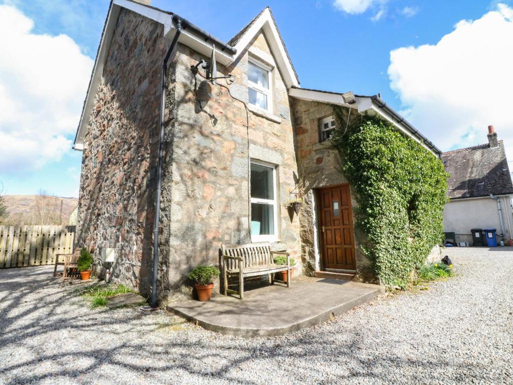 una casa de piedra con un banco delante en The Knowe Lower, en Taynuilt