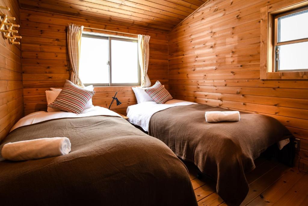 two beds in a log cabin with a window at Betsu Inn in Hakuba