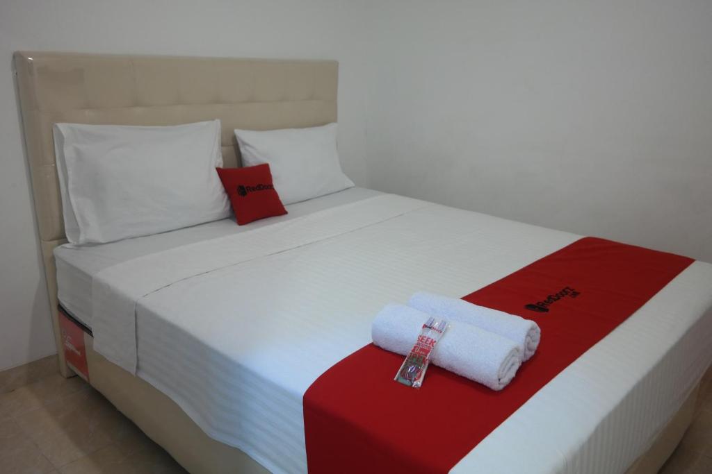 uma cama branca com toalhas vermelhas e brancas em RedDoorz near Mall Ratu Indah 3 em Balangberu