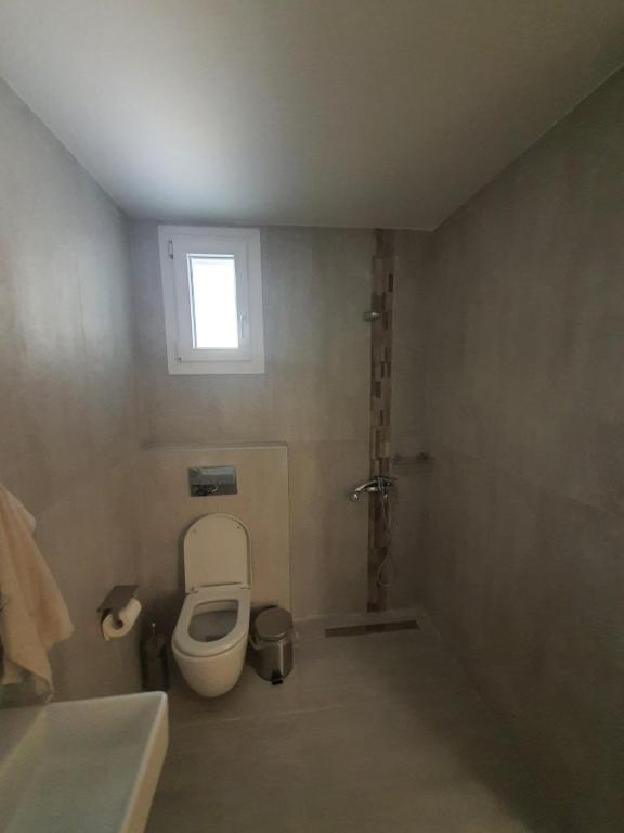 mała łazienka z toaletą i oknem w obiekcie New apartment ,50m from the sea at Nea Irakleia. w mieście Nea Iraklia