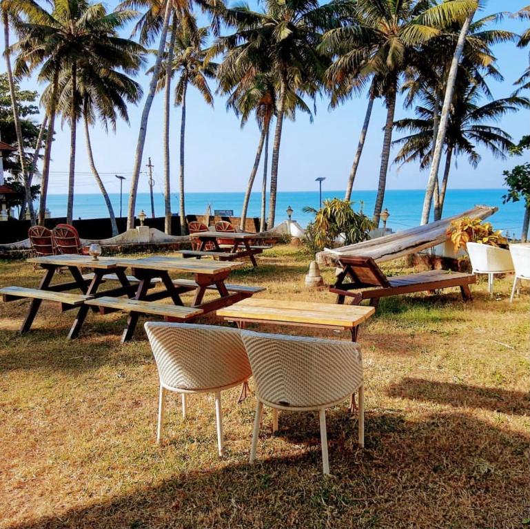 un grupo de mesas de picnic en la playa con palmeras en Vibes Beach House, en Varkala
