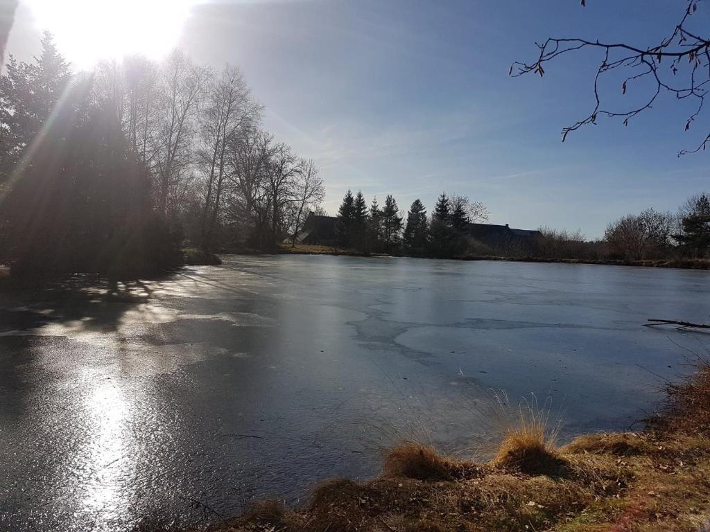 a frozen lake with the sun shining on it at Fermette typique auvergnate dans son écrin d'eau et de verdure in Saint-Donat