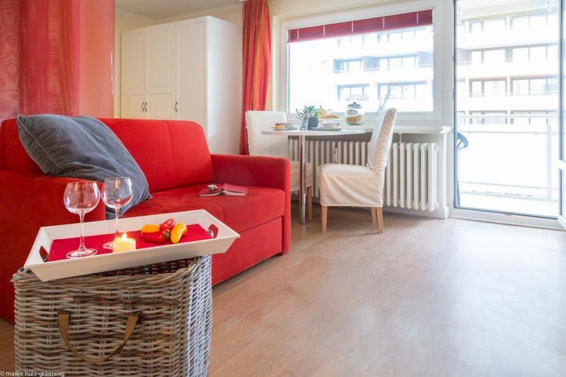 Ad5 305 Dwarsloeper 1 في فيسترلاند: غرفة معيشة مع أريكة حمراء وطاولة مع كؤوس للنبيذ