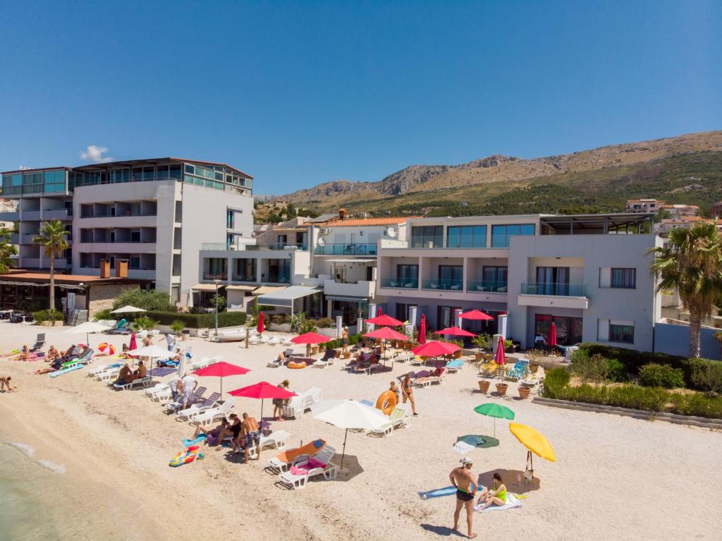 un groupe de personnes assises sur une plage avec des parasols dans l'établissement Luxury rooms Beach Mediteran, à Podstrana