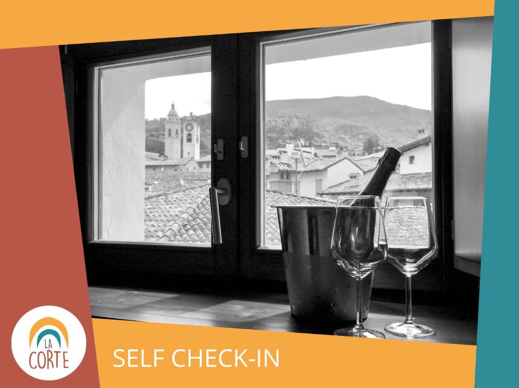 a bottle of wine and two glasses on a table with a window at La Corte Room & Relax in Rovereto