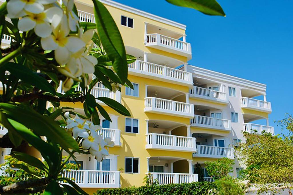 een geel gebouw met witte balkons en een boom bij Blue Bay Beach Apartment in Blauw Baai