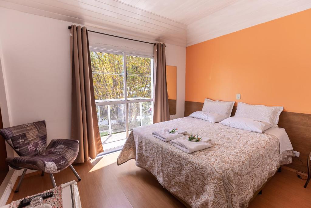a bedroom with a bed with a window and a chair at Hotel Geneve in Campos do Jordão