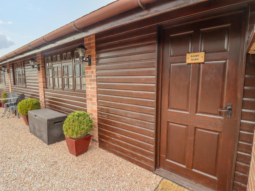 a large wooden garage with a door and some plants at Dairy Barn in Pershore