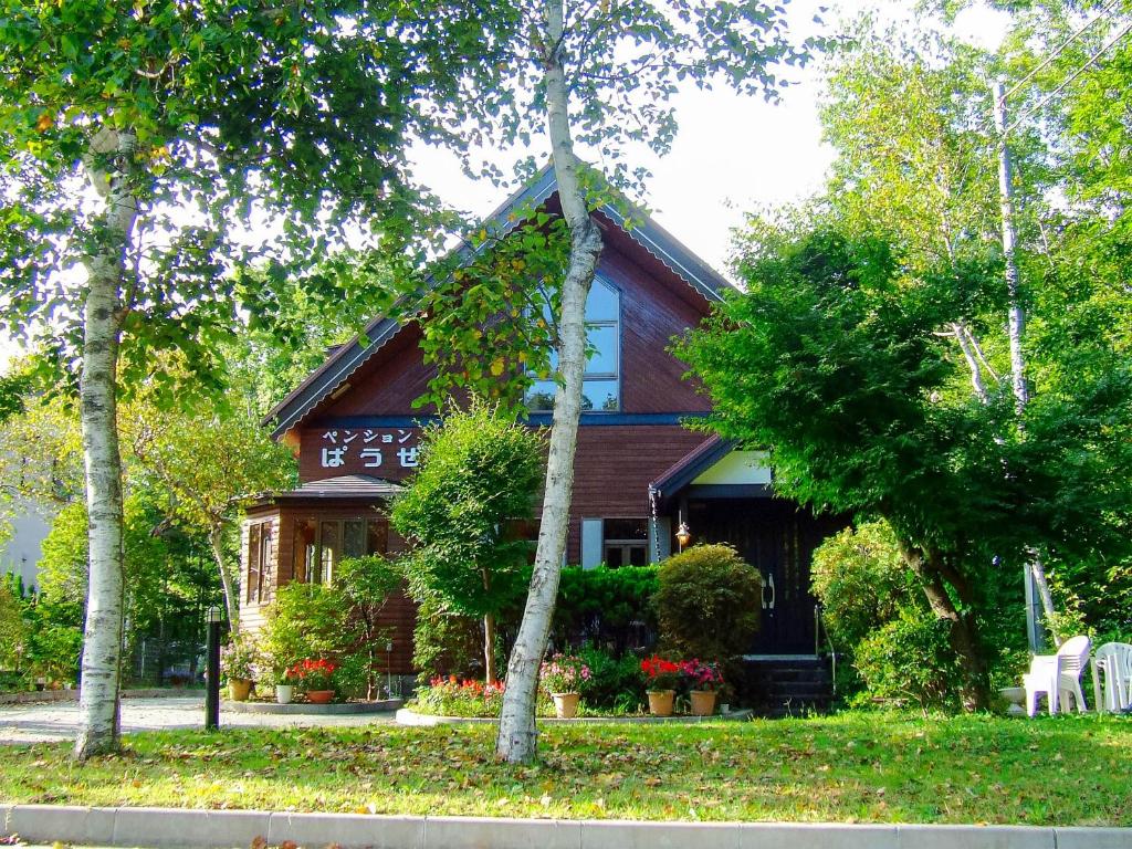 una casa con techo de gambrel con flores y árboles en Yamanakako Pension Pause, en Yamanakako