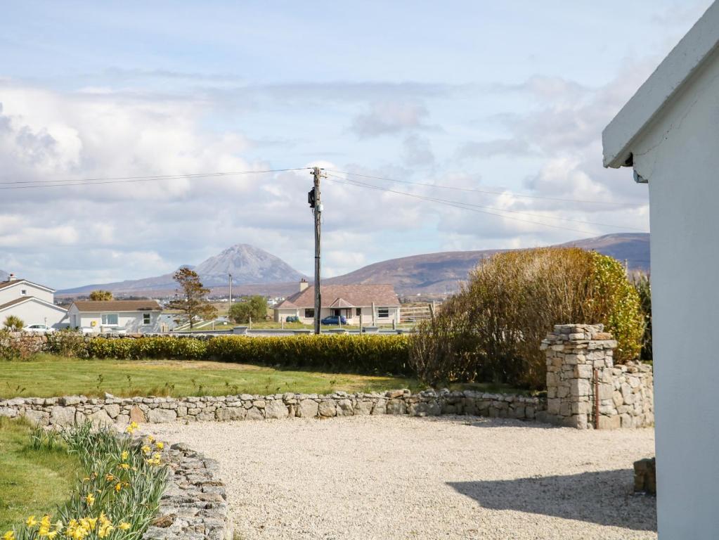 a house with a stone wall and mountains in the background at Radharc na nOileán in Kincasslagh