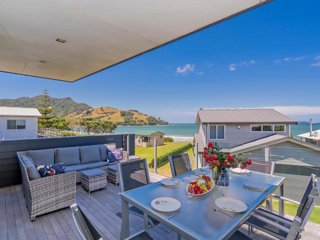 a table and chairs on a deck with a view of the ocean at Breezy Views - Simpsons Beach Holiday Home in Whitianga