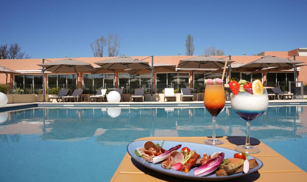 une assiette de nourriture et deux boissons sur une table à côté d'une piscine dans l'établissement Mount Venturi - Aix-En-Provence Sainte-Victoire - Bar & Restaurant & Padel, à Rousset
