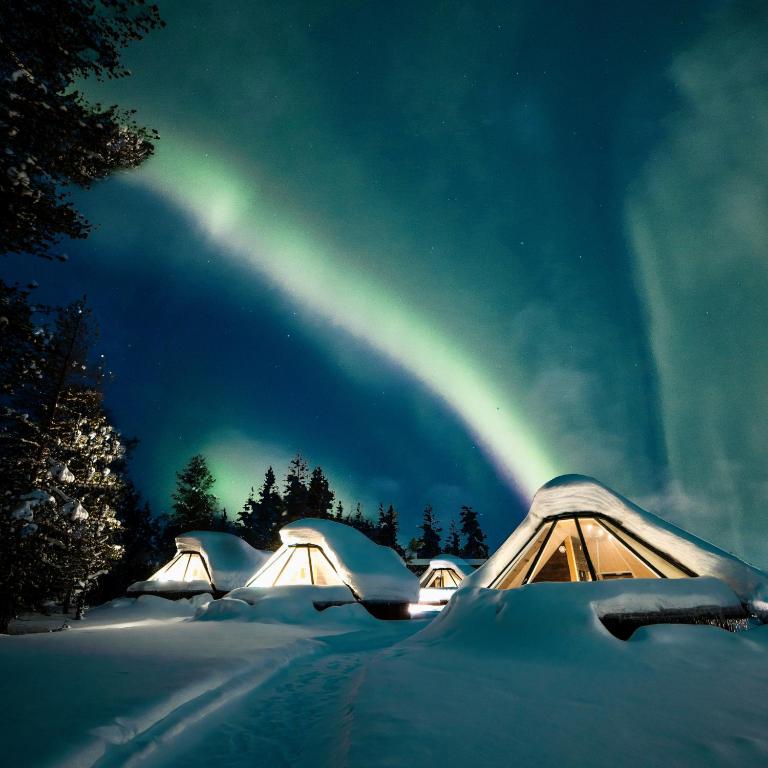 a group of tents in the snow with a rainbow in the sky at Wilderness Hotel Nellim & Igloos in Inari