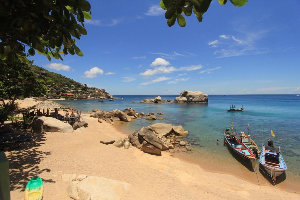 two boats on a beach with rocks and water at Mountain Reef Beach Resort in Koh Tao