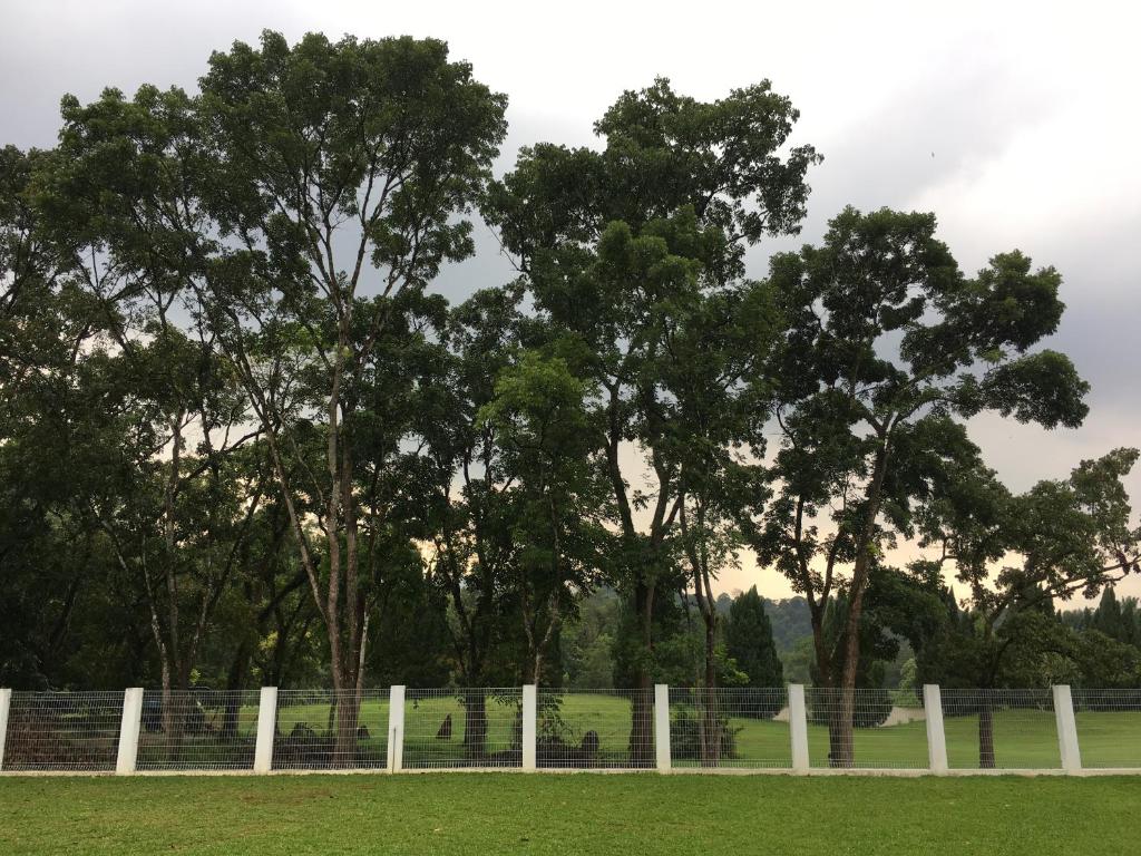 einen Zaun auf einem Feld mit Bäumen im Hintergrund in der Unterkunft Ode to Joy in Serendah