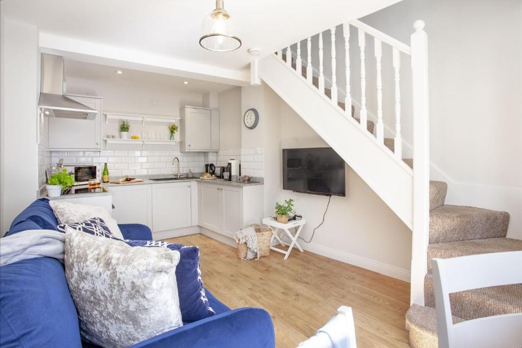 a living room with a blue couch and a kitchen at Cobblers Cottage in Sidmouth