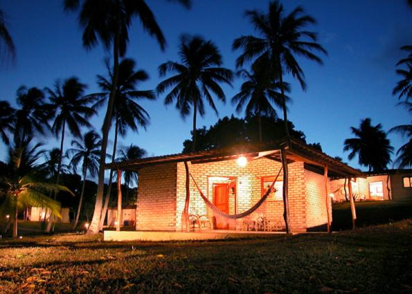 a house with a hammock outside of it with palm trees at Barravilha Chales in Barra do Cunhau