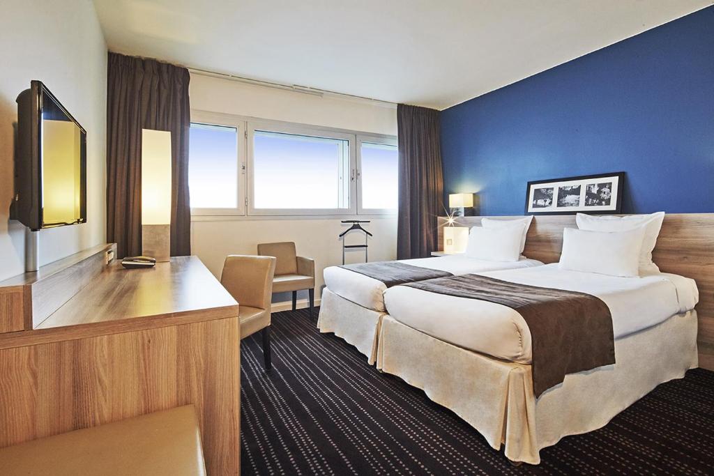 ein Hotelzimmer mit einem großen Bett und einem Schreibtisch in der Unterkunft Campanile Le Bourget – Airport in Le Bourget